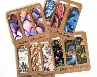 Può includere: Una collezione di segnalibri rettangolari fissati su un supporto di cartone marrone con il testo Happy Reading. I disegni includono scaglie di drago viola, un drago rosso, un drago blu, mappe fantasy, una foresta scura, un cottage e funghi.