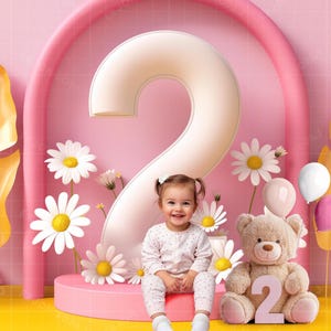 Puede incluir: Un niño pequeño se sienta frente a un gran número dos blanco, rodeado de margaritas blancas y globos rosas. El niño lleva una camisa de lunares blancos y rosas y pantalones rosas. Un oso de peluche con un número dos en el pecho se sienta junto al niño.