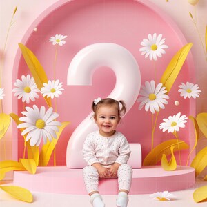 Puede incluir: Una niña pequeña con un mono blanco con lunares rosas se sienta frente a un gran número dos blanco. El número dos está frente a un fondo rosa con margaritas blancas y hojas amarillas.