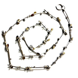 May include: A silver necklace with a delicate chain and small leaf-shaped charms. The necklace is made of metal and has a simple, elegant design.