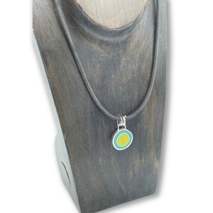 May include: A black cord necklace with a silver pendant featuring a yellow circle surrounded by a turquoise ring.