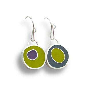 May include: A pair of silver dangle earrings with round resin charms. One charm is green with a purple circle inside, the other is gray with a green circle inside.