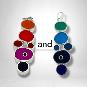 May include: Two silver-toned earrings with colorful, abstract designs. One earring features orange, red, burgundy, purple, and black shapes. The other has green, blue, navy, and indigo shapes. The word "and" is between them.