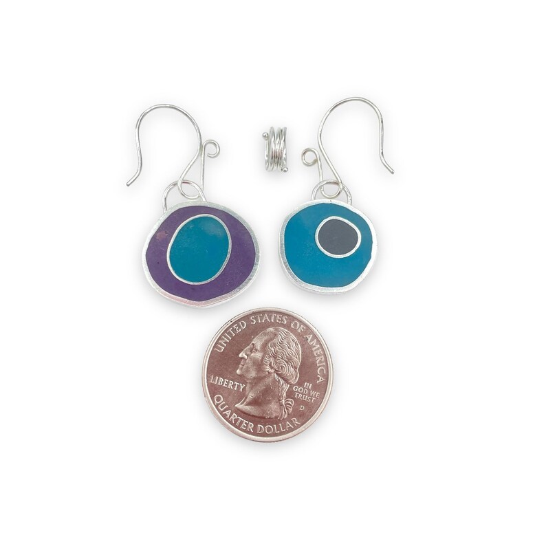 May include: A pair of silver earrings with a teal and purple enamel design. The earrings are about the size of a quarter.