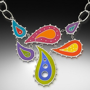 May include: A silver necklace with a colorful paisley design. The necklace features six teardrop-shaped pendants with different colors and patterns, including pink, orange, yellow, green, blue, and purple.