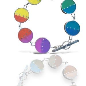 May include: A silver bracelet with colorful round charms. Each charm is divided in half with a different color on each side. The charms are connected by a silver chain. The bracelet has a silver toggle clasp.