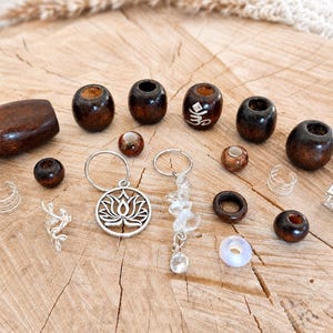 May include: A collection of hair accessories including dark brown wooden beads, silver-toned metal cuffs, a silver-toned lotus flower charm hoop, and a silver-toned hoop with clear crystal beads. One wooden bead features a white Om symbol.