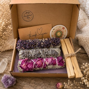 Peut inclure: Une boîte cadeau en carton contenant trois bouquets d'herbes et de fleurs séchées, dont de la lavande et des pétales de rose, liés avec de la ficelle blanche. Deux bâtonnets en bois clair, une carte de remerciement et un autocollant solaire.