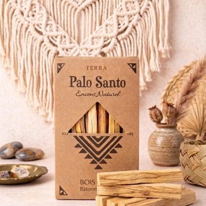 Può includere: Una scatola di cartone con bastoncini di incenso Palo Santo, con il testo "TERRA Palo Santo Encens Naturel" e un motivo geometrico. Diversi bastoncini sono visibili fuori dalla scatola. Lo sfondo include un arazzo tessuto e oggetti decorativi.
