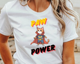 May include: White t-shirt with a graphic of a cat dressed as a superhero with a red cape and the text "PAW POWER" in yellow and black letters.
