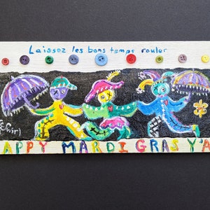 May include: A colorful painting on wood with three jester figures holding umbrellas. The painting has the text "Laissez les bons temps rouler" and "HAPPY MARDI GRAS Y'ALL" in colorful letters.