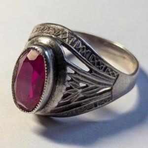 May include: Silver-toned ring featuring an oval, deep red gemstone. The ring has an ornate, openwork design on the band and around the gemstone setting. The gemstone is the focal point, set in a detailed, vintage-style mounting.