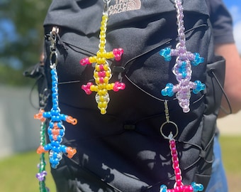 Può includere: Quattro portachiavi a forma di lucertola perlate appese a uno zaino nero. Le lucertole sono gialle, blu, viola e rosa con accenti blu e bianchi.