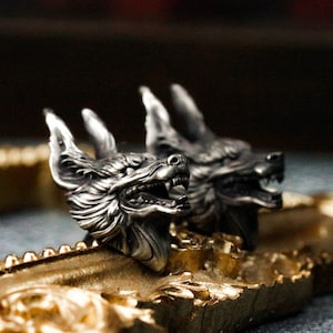 May include: Two silver wolf head sculptures with open mouths and sharp teeth, resting on a gold-coloured frame.