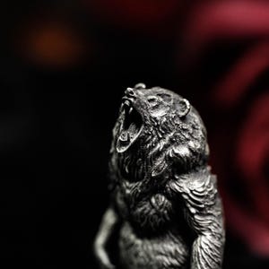 May include: A detailed, silver-colored bear figurine with its mouth open in a roar. The sculpture has a textured surface, capturing the fur and facial features. The background is dark, with a hint of red.