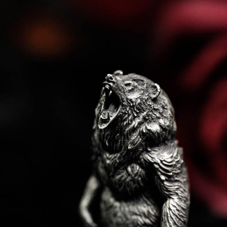 May include: A detailed, silver-colored bear figurine with its mouth open in a roar. The sculpture has a textured surface, capturing the fur and facial features. The background is dark, with a hint of red.