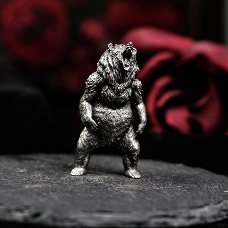 May include: A detailed silver-colored bear figurine, standing upright with its mouth open in a roar. The bear has textured fur and is set against a dark background with a hint of red.
