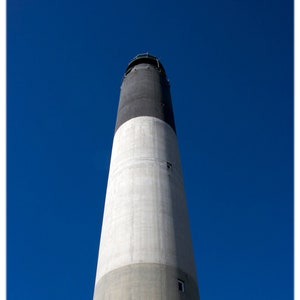 Op de afbeelding: Een hoge, witte en zwarte vuurtoren tegen een helderblauwe lucht.
