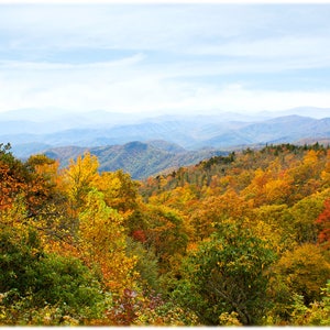 Peut inclure: Une vue panoramique d'une chaîne de montagnes avec des feuillages d'automne dans des tons de rouge, orange, jaune et vert. Les montagnes sont superposées au loin, avec un ciel bleu et des nuages blancs au-dessus.