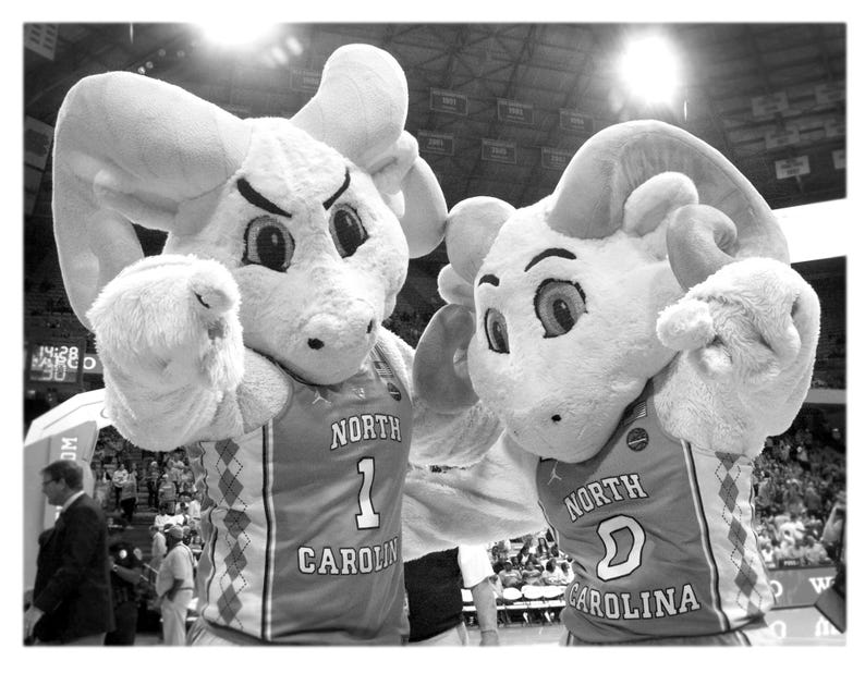 Puede incluir: Dos mascotas con uniformes de baloncesto. La mascota de la izquierda es una criatura peluda blanca con un hocico largo y orejas grandes. La mascota de la derecha es una criatura peluda blanca con un hocico largo y grandes cuernos. Ambas mascotas llevan camisetas que dicen "North Carolina" y tienen un n&uacute;mero en la parte delantera. La mascota de la izquierda tiene el n&uacute;mero "1" y la mascota de la derecha tiene el n&uacute;mero "0".