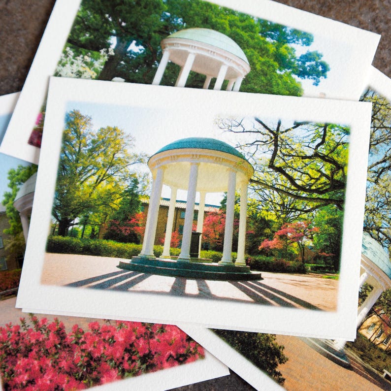 May include: A stack of white postcards featuring a photograph of a classical gazebo with a teal dome and white columns. The gazebo is surrounded by trees and greenery, with long shadows cast on the ground. Other postcards are visible.