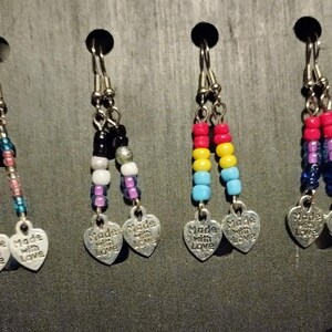 May include: A collection of beaded earrings with silver-toned heart charms that read "Made with Love." The earrings feature various color combinations, including rainbow, pink, blue, and black beads.