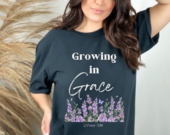 May include: Black t-shirt with white text that reads "Growing in Grace" and a floral design with purple flowers and butterflies. The text "2 Peter 3:18" is below the floral design.