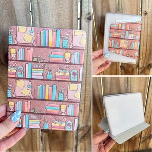May include: A decorative e-reader case featuring a bookshelf design with colorful books, flowers, and the letters "TBR". The case is pink with a repeating pattern and is shown in multiple views.