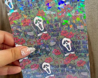 May include: Holographic sticker with a repeating pattern of a ghost face, roses, and text that reads "You Had Me at Masked Men." The sticker has a dark background with a shiny, iridescent finish.