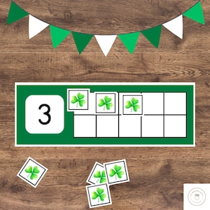 Puede incluir: Una herramienta educativa con temática del Día de San Patricio que presenta una pancarta verde y blanca, el número 3 en verde y blanco e ilustraciones de tréboles. La herramienta está diseñada para enseñar a contar y reconocer números. Hay tarjetas de tréboles adicionales.