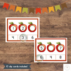 May include: A set of 10 printable clip cards featuring red apples with numbers on them. The cards are designed for early math learners to practice counting and number recognition. The text "10 clip cards included" is at the bottom of the image.
