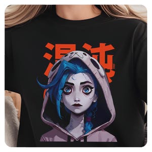 May include: Black t-shirt with a graphic of a cartoon character with blue hair and a pink hoodie. The character has a sad expression and is wearing a white headband with a paw print. The text "Jinx" and Japanese characters are printed in orange on the shirt.