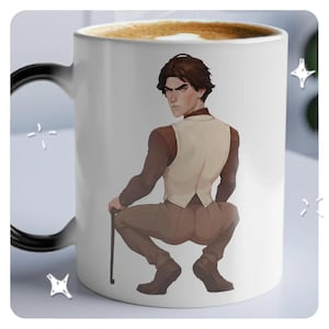 Op de afbeelding: Een witte keramische mok met een zwart handvat. De mok heeft een gekleurde illustratie van een persoon in een bruin pak en vest, die een stok vasthoudt, met de rug naar de kijker.