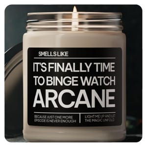 Peut inclure: Une bougie allumée, de couleur blanc cassé, dans un pot en verre avec une étiquette noire. L'étiquette indique "Smells Like It's Finally Time To Binge Watch Arcane". Le texte en dessous dit "Because Just One More Episode Is Never Enough" et "Light Me Up And Let The Magic Unfold."