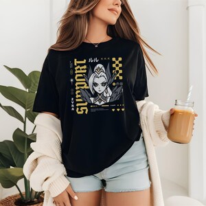 以下が含まれることがあります： 黒いTシャツ。金色のグラフィックデザインで、アニメ風のキャラクターと「SUPPORT」の文字が描かれています。デザインには日本語のテキストと幾何学模様が含まれています。Tシャツは人が着ています。
