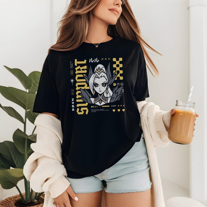 以下が含まれることがあります： 黒いTシャツ。金色のグラフィックデザインで、アニメ風のキャラクターと「SUPPORT」の文字が描かれています。デザインには日本語のテキストと幾何学模様が含まれています。Tシャツは人が着ています。