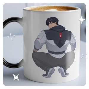 May include: White ceramic coffee mug featuring a color illustration of a person in a gray and white jacket with a black hood. The mug has a black handle and is filled with coffee.