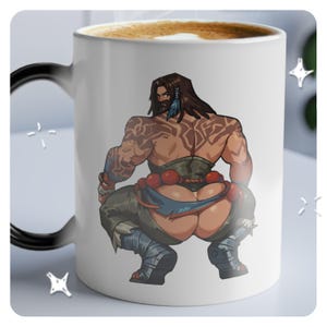 May include: White ceramic mug with a black handle. The mug features a cartoon illustration of a muscular, tattooed person with long brown hair, wearing a brown and blue outfit. The person is facing away from the viewer and is in a squatting position.
