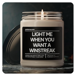 May include: A brown glass candle jar with a black label that reads "LIGHT ME WHEN YOU WANT A WINSTREAK". The label also includes the text "WARNING: MAY INDUCE TIME LOSS AND UNSTOPPABLE CHAIN WINS" and "THE SCENT OF FLAWLESS OUTPLAYS".
