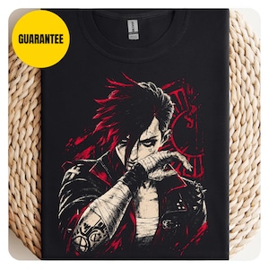 Può includere: Una t-shirt nera a girocollo con un'illustrazione grafica di un personaggio dai capelli corti e scuri, che indossa una giacca scura con borchie. Il design utilizza una tavolozza di colori rosso e nero con accenti bianchi, mostrando mani fasciate.