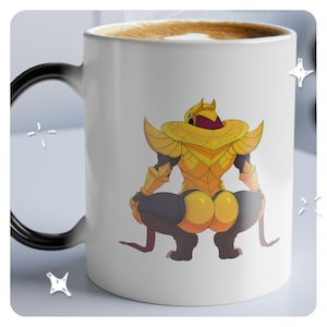 May include: White ceramic mug featuring a cartoon character in golden armor. The character is squatting, with a detailed design on the back. The handle is black, and the mug contains a brown liquid.