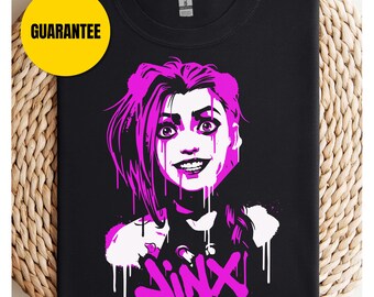 May include: Black t-shirt with a graphic of a character with pink hair and the name "JINX" in graffiti style. The design has white accents and a yellow "GUARANTEE" circle. The t-shirt is a bold, graphic design.