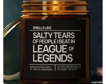 Puede incluir: Un tarro de vela de vidrio marrón con una tapa dorada y una etiqueta negra que dice "Smells Like Salty Tears of People I Beat in League of Legends". La etiqueta también incluye el texto "Burns hotter than a 20-minute surrender" y "Victory never smelled so sweet, or salty".