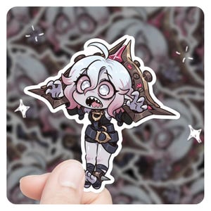 May include: A sticker featuring a cartoon character with pink hair, white eyes, and a wide open mouth. The character is wearing a black and gold outfit and has a large, dark brown wing behind it.