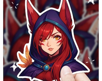 May include: A sticker featuring a stylized anime-style character with red hair and fox-like ears, wearing a blue hooded cloak. The character has yellow eyes and is adorned with a gold feather. The sticker is held by a hand.