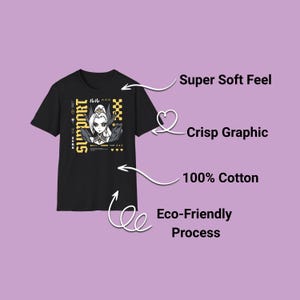 以下が含まれることがあります： 女性アニメキャラクターのグラフィックが描かれた黒いTシャツ。「SUPPORT」の文字が黄色で、日本語のテキストも入っています。画像には「Super Soft Feel」、「Crisp Graphic」、「100% Cotton」、「Eco-Friendly Process」の文字も含まれています。