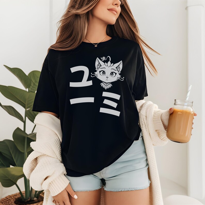 May include: Black t-shirt with a white graphic of a cat face and Japanese characters. The cat has large eyes and a crown. The shirt is a casual style.