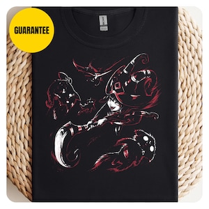 May include: A black t-shirt featuring a graphic print of a character wearing a large hat and wielding a curved scythe, surrounded by small shadowy creatures. The design uses red and white ink on the black fabric, with a yellow circle containing the text GUARANTEE.