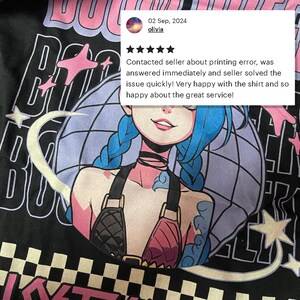 May include: Black t-shirt featuring a colorful anime-style illustration of a woman with blue hair. The design includes stars and the text "BU". A customer review is visible in the upper right corner.