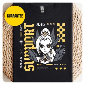 以下が含まれることがあります： キャラクターのイラストと黄色で「SUPPORT」という文字が描かれた黒いTシャツ。デザインには日本語のテキストと「ZYRA」という文字が含まれています。左上には黄色の「保証」の円があります。Tシャツは織り込まれた背景にあります。